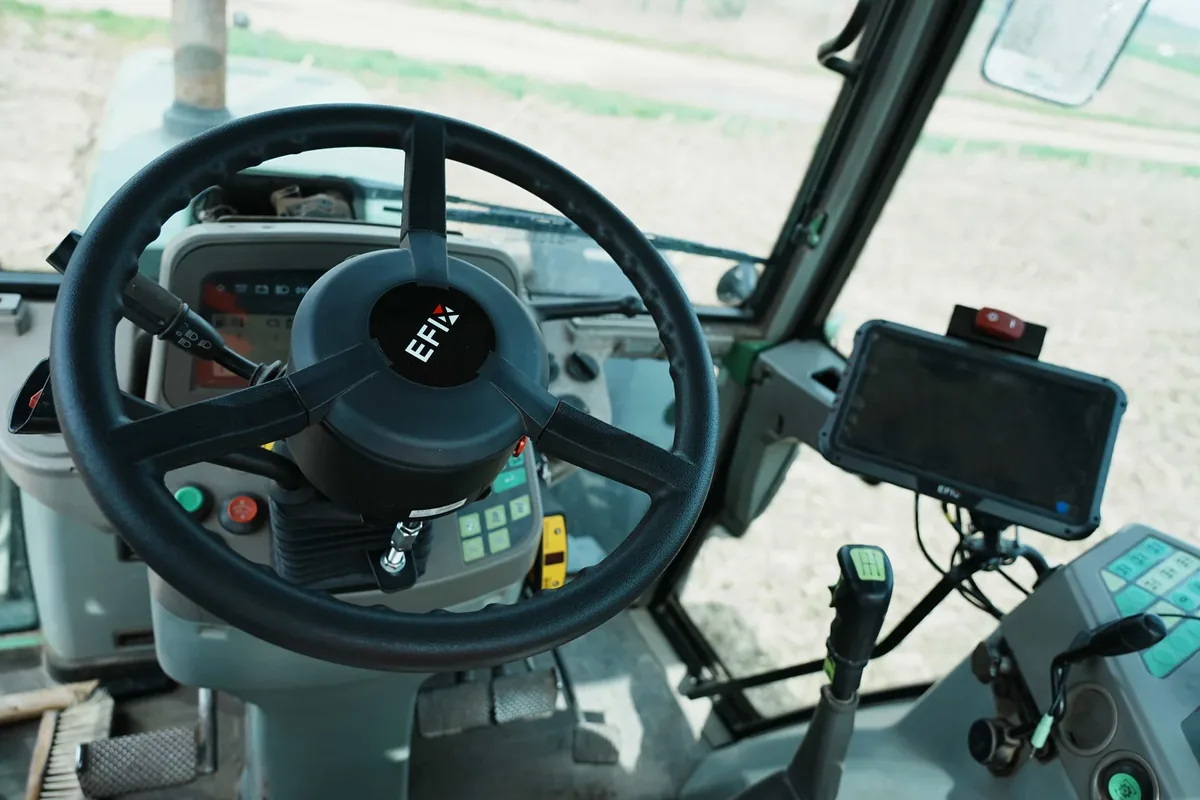 Cabina d'un tractor amb el volant elèctric EFIX muntat en lloc del de sèrie i la pantalla de l'autoguiat a la dreta, i el camp al fons