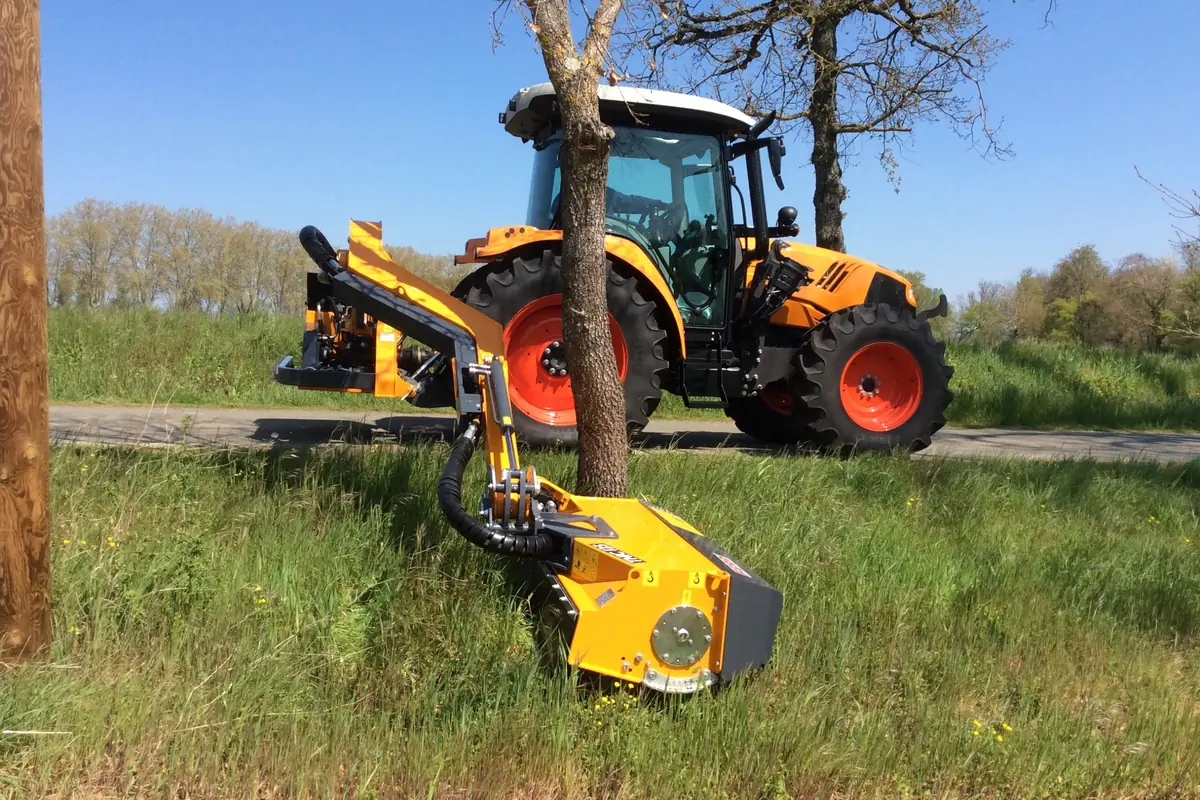 Braç desbrossador Ferri arribant al voltant del tronc d'un arbre, amb el capçal a ran de terra i herba alta al davant