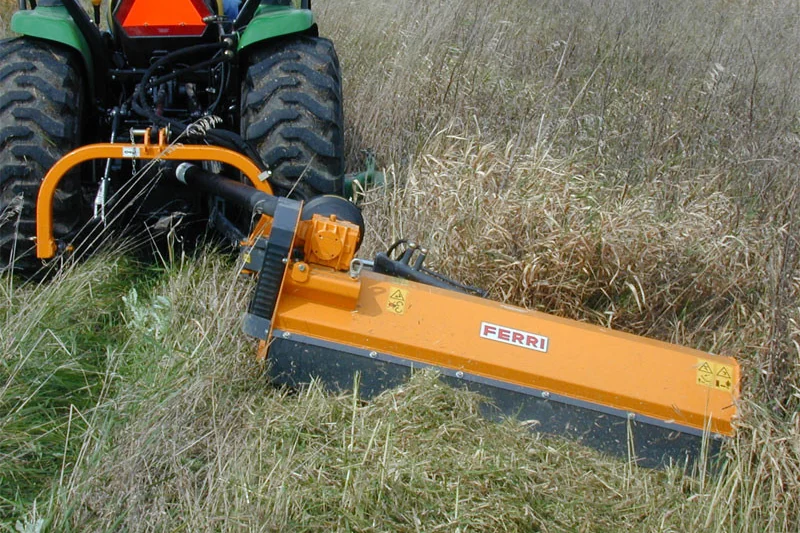Desbrossadora Ferri groga de prop, segant herba alta darrere d'un tractor verd