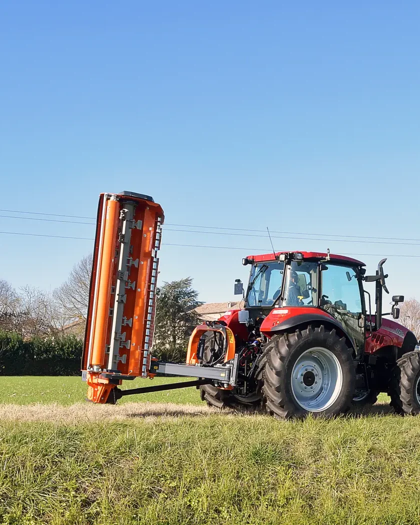 Tractor vermell amb una desbrossadora Ferri taronja aixecada al costat, a la vora d'un canal, amb el cel blau al damunt