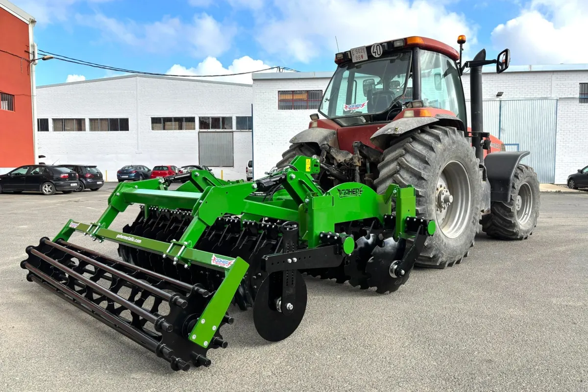 Grada ràpida Gaher enganxada a un tractor vermell, davant d'una nau industrial