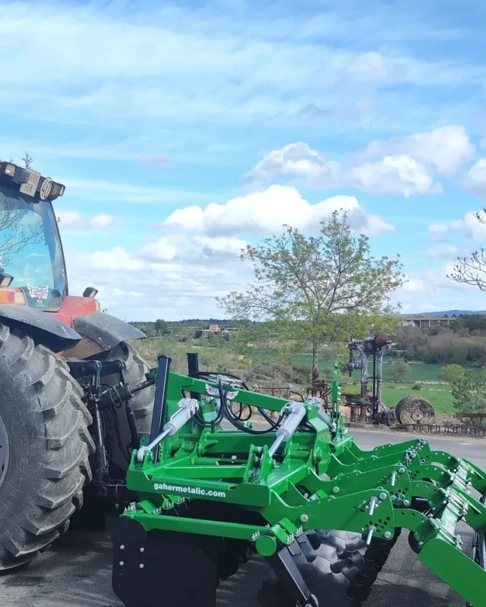 Grada ràpida Gaher enganxada a un tractor vermell, aturada a l'aire lliure sota un cel amb núvols