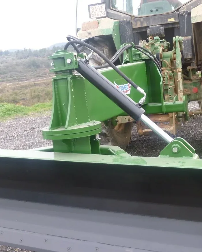 Pala polidozer Gaher verda muntada al darrere d'un tractor verd, inclinada i a punt de treballar sobre un camí de grava