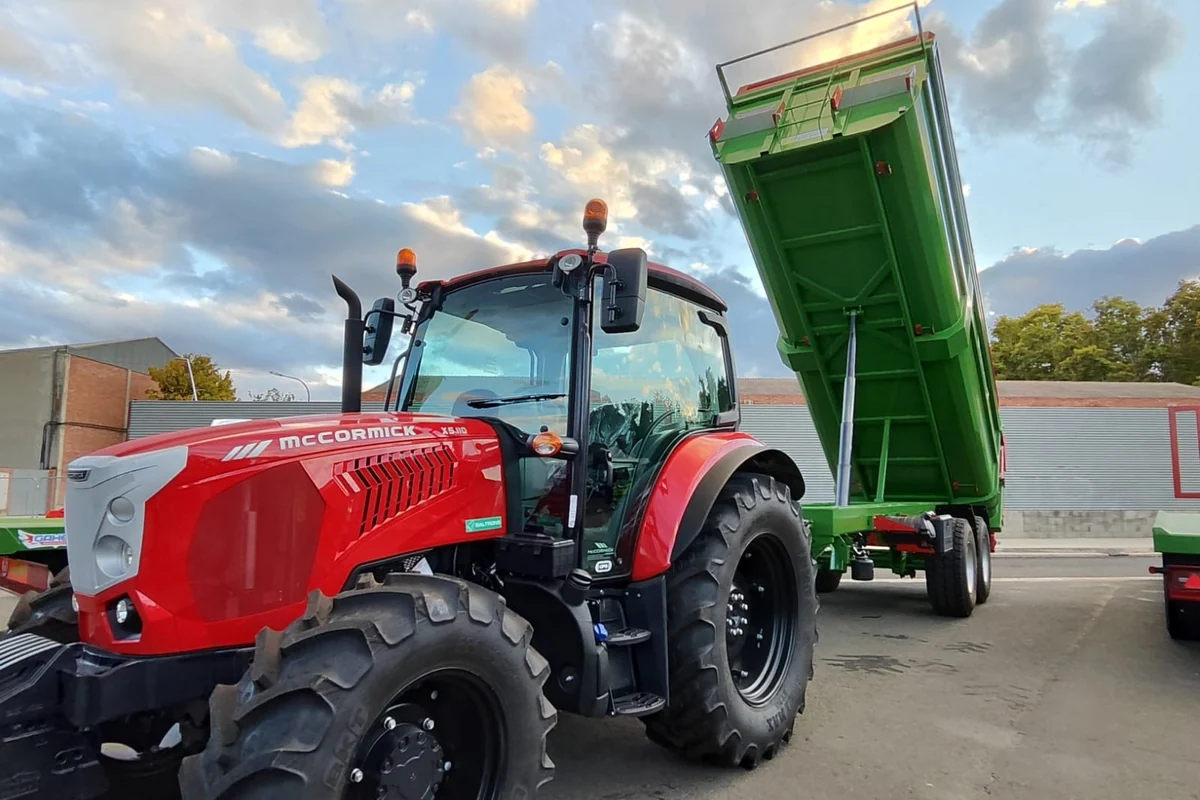 Banyera Gaher verda amb la caixa aixecada darrere d'un tractor vermell, en un pati