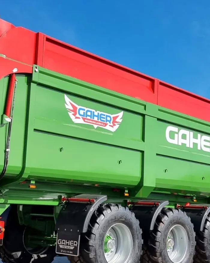 Banyera Gaher de tres eixos amb la caixa verda i les vores vermelles, a l'aire lliure sota un cel blau