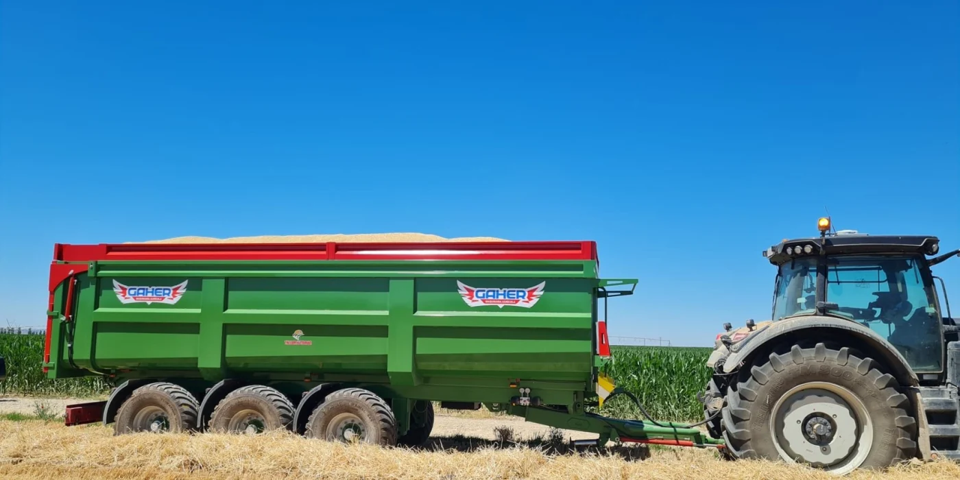 Banyera Gaher de tres eixos carregada de gra fins dalt, enganxada a un tractor en un camp de rostoll amb blat de moro al fons