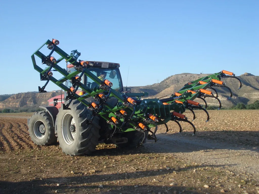 Semixissel Gaher amb les ales aixecades darrere d'un tractor vermell, en un camp amb turons al fons