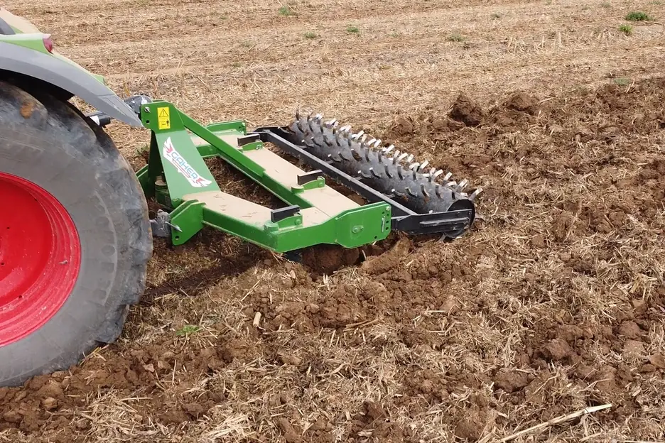 Subsolador Gaher treballant terra remoguda darrere d'un tractor de rodes vermelles, amb el corró de pues al darrere