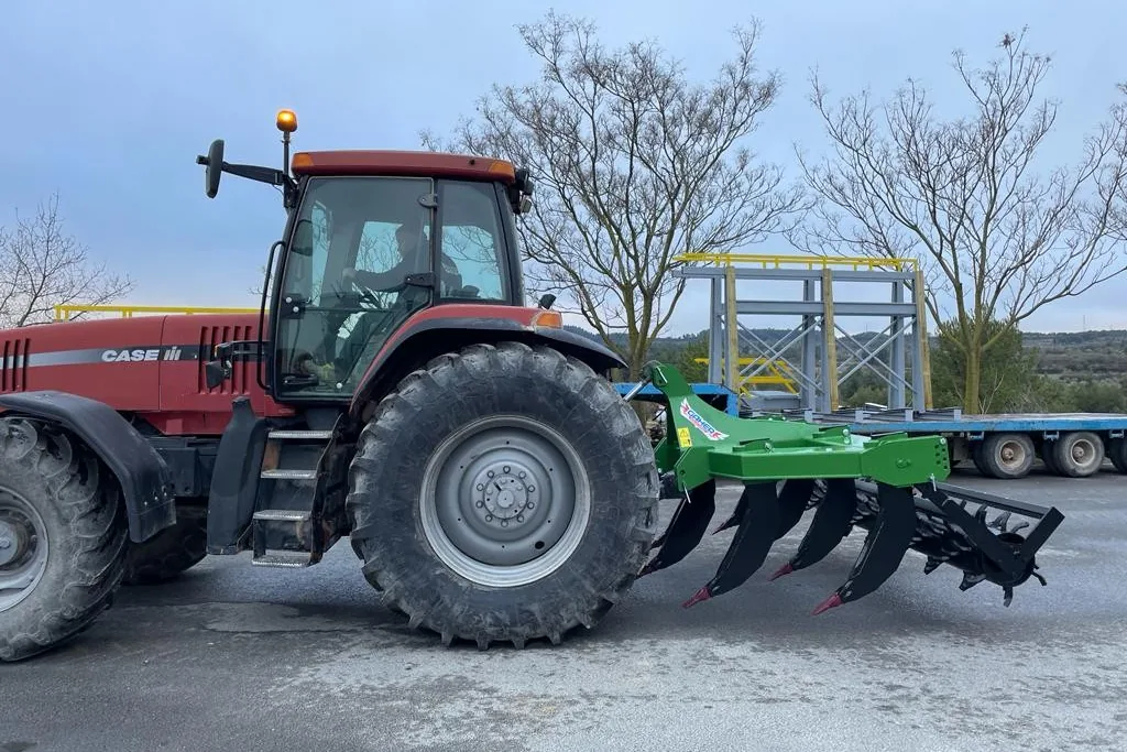 Tractor vermell amb un subsolador Gaher enganxat al darrere, de perfil, en un pati