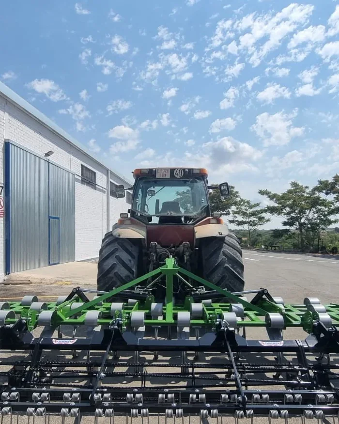 Vibrocultor Gaher desplegat a tota amplada darrere d'un tractor, davant d'una nau blanca i sota un cel amb núvols