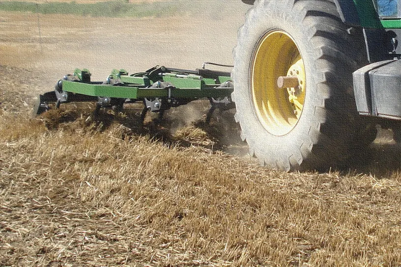 Xissel Gaher treballant un rostoll darrere d'un tractor de rodes grogues, aixecant pols