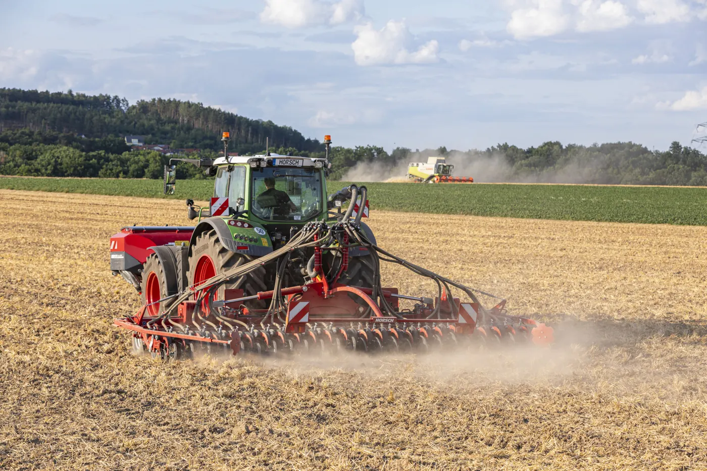 Sembradora Horsch Avatar sembrant amb pols darrere d'un tractor verd, amb una recol·lectora treballant al fons