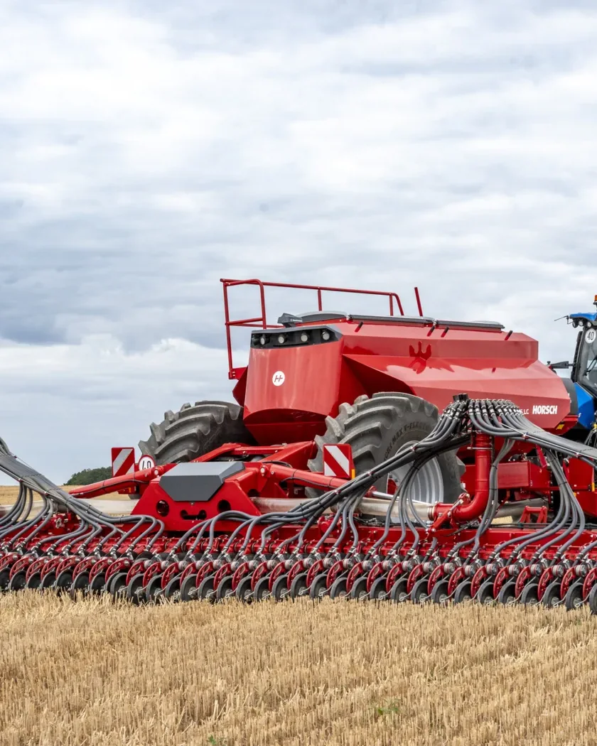Sembradora Horsch Avatar desplegada a tota amplada darrere d'un tractor blau, sobre un camp de rostoll