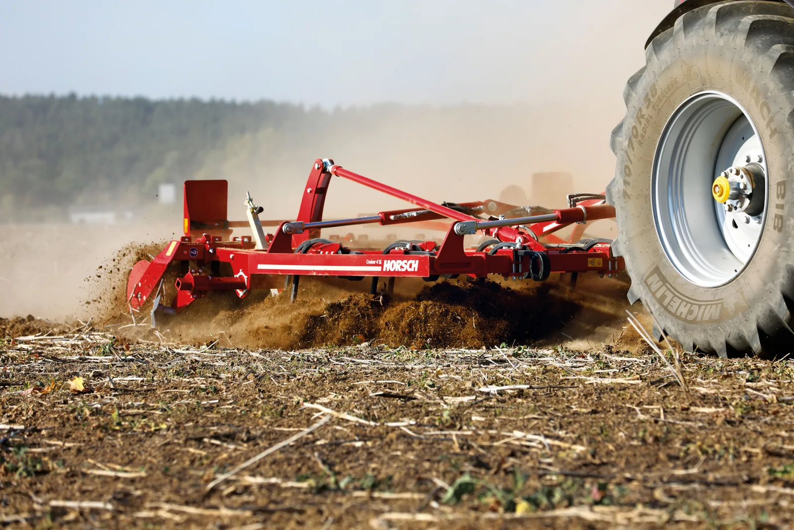 Cultivador Horsch Cruiser treballant a ras de terra, amb la roda del tractor en primer terme i la terra saltant