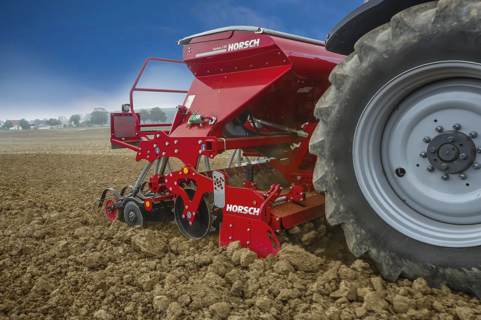 Primer pla de la grada rotativa de l'Express amb la roda del tractor al costat, sobre un sòl de terrossos