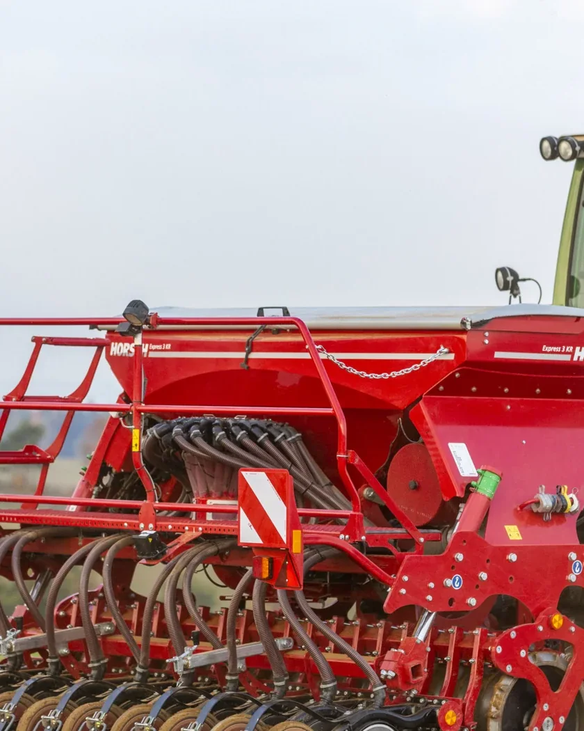 Sembradora Horsch Express amb la tremuja vermella, enganxada a un tractor verd sobre un camp treballat