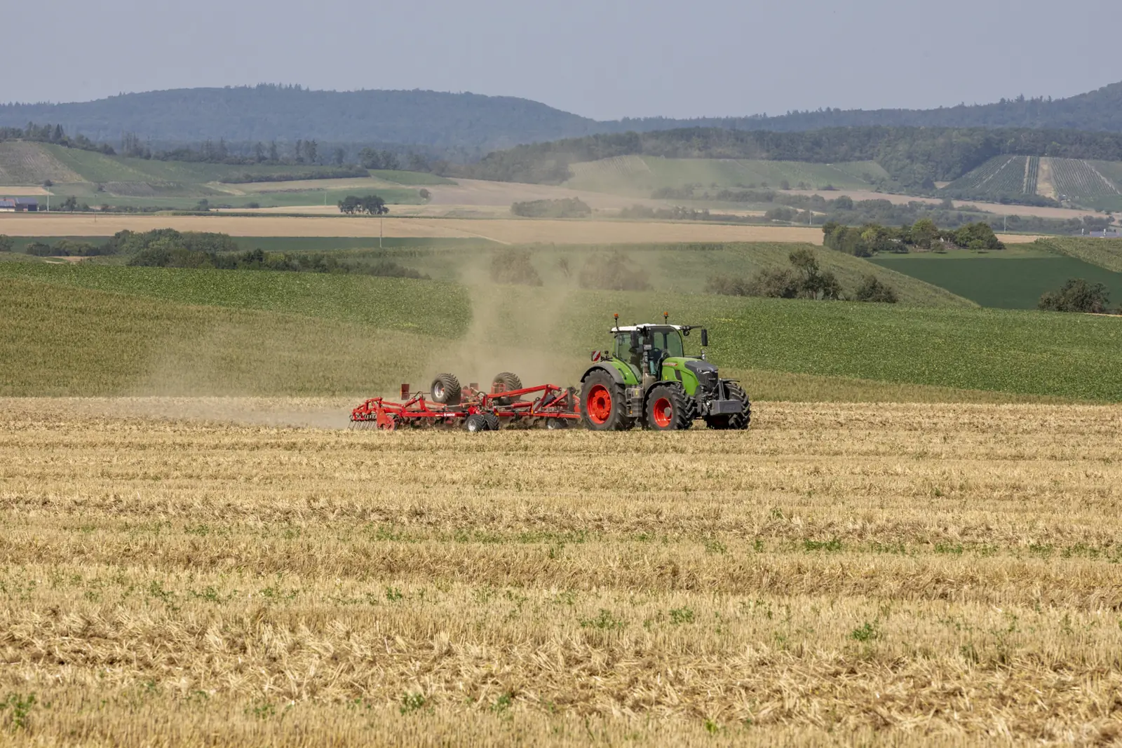 Tractor verd amb un Finer treballant en un camp de rostoll, amb les muntanyes i els boscos al fons