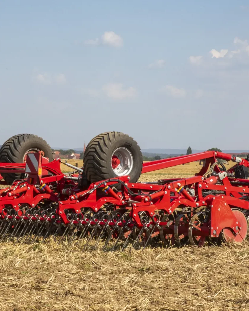 Cultivador Horsch Finer desplegat darrere d'un tractor verd, sobre un camp de rostoll amb els turons al fons