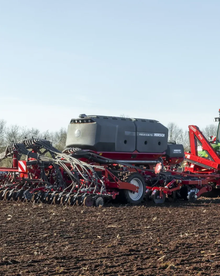Sembradora Horsch Focus amb la tremuja fosca, enganxada a un tractor verd sobre un camp de terra treballada