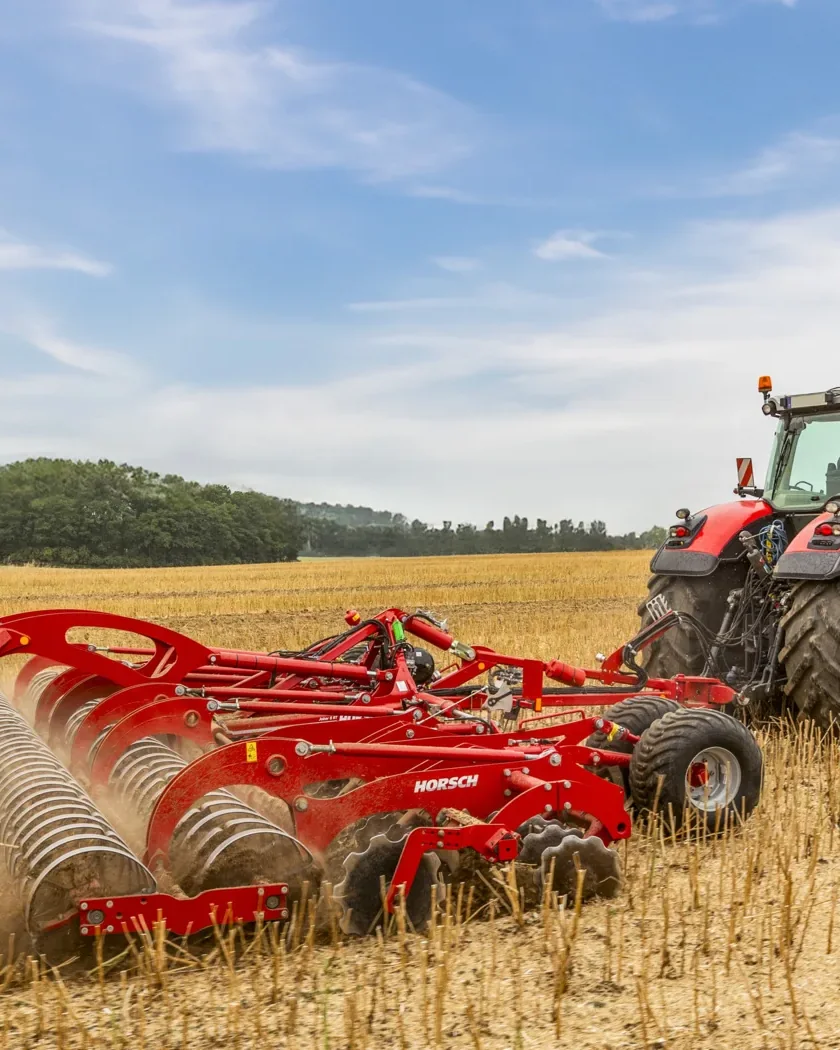 Grada de discos Horsch Joker RT desplegada sobre rostoll de cereal, estirada per un tractor, amb el cel obert al damunt