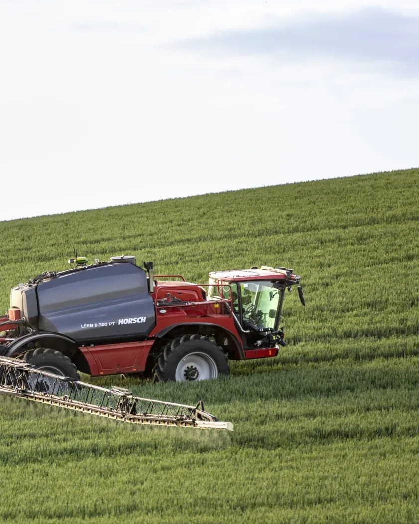 Polvoritzador autopropulsat Horsch Leeb 8.300 PT amb la barra desplegada, treballant en un camp de cereal verd en pendent