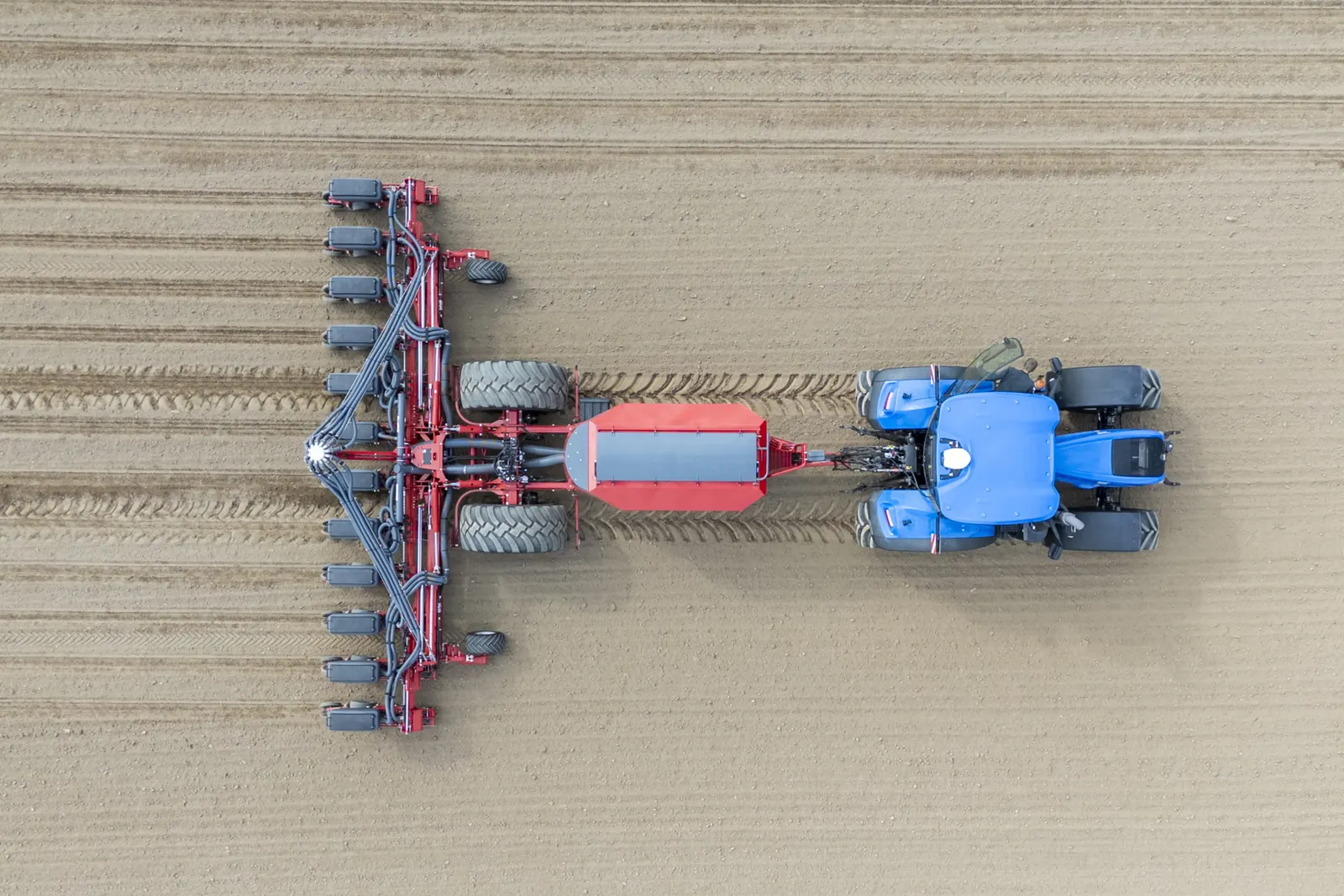 Vista des de dalt d'un tractor blau amb la sembradora Maestro desplegada sobre un camp acabat de sembrar