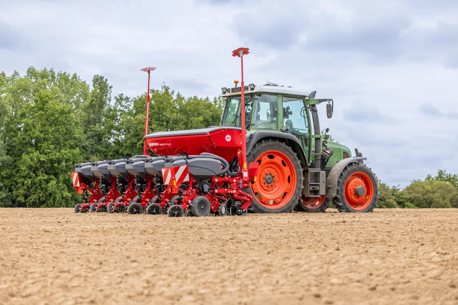 Sembradora Horsch Maestro darrere d'un tractor verd, amb la filera d'elements de sembra i el bosc al fons