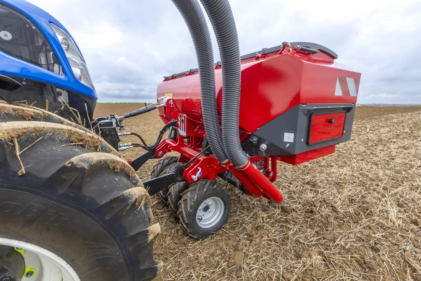 Primer pla de la tremuja Partner al davant d'un tractor blau, amb les dues mànegues d'aire i el rostoll al fons