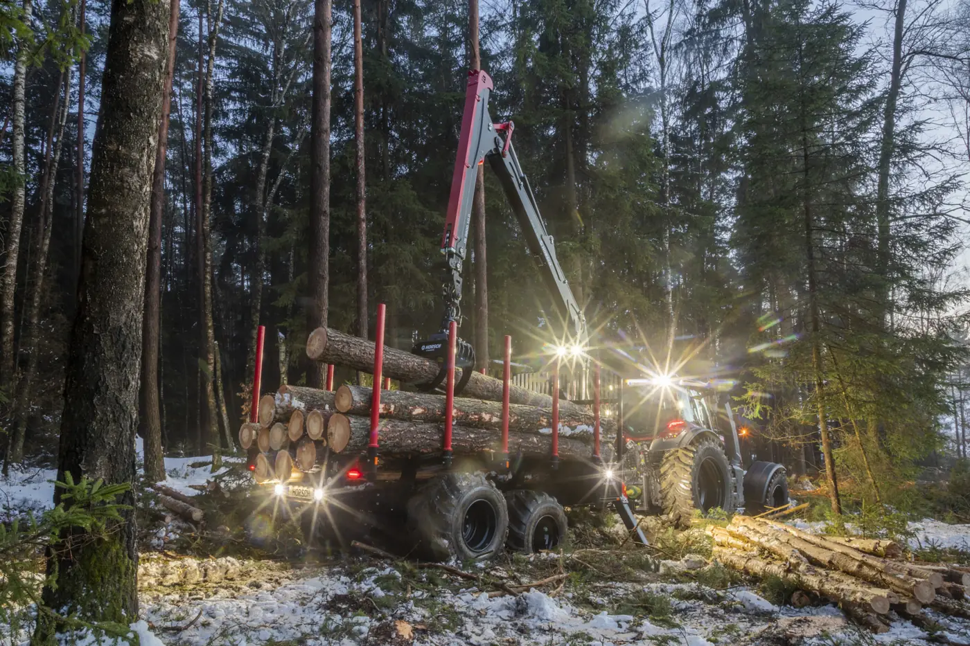 Remolc forestal Horsch Pirk treballant amb els fars encesos en un bosc nevat, a contrallum