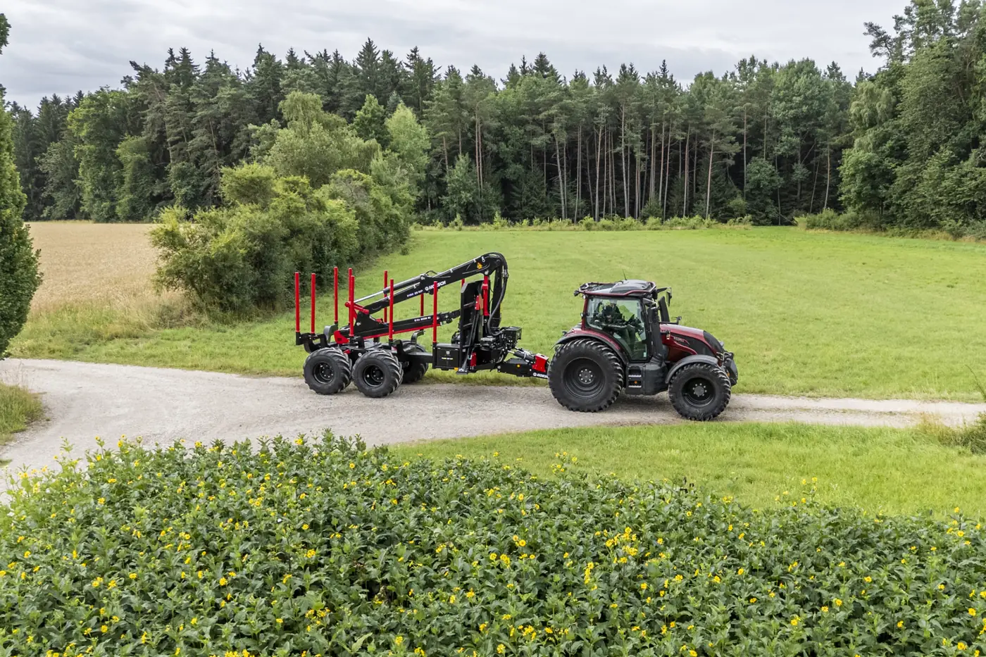 Tractor amb el remolc Pirk buit i la grua plegada, en una corba d'un camí entre prats i bosc