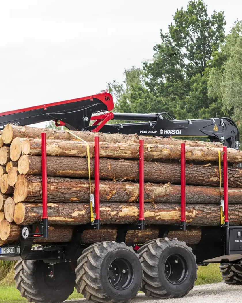 Tractor amb el remolc forestal Horsch Pirk carregat de troncs, circulant per un camí amb el bosc al fons