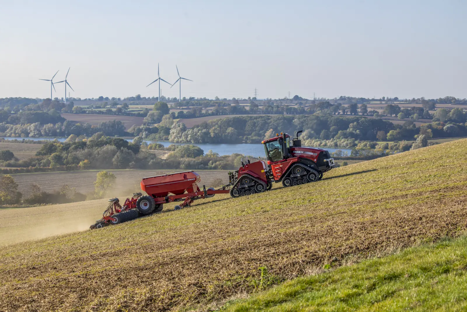Tractor d'erugues amb una Serto treballant en un vessant, amb els aerogeneradors i l'aigua al fons