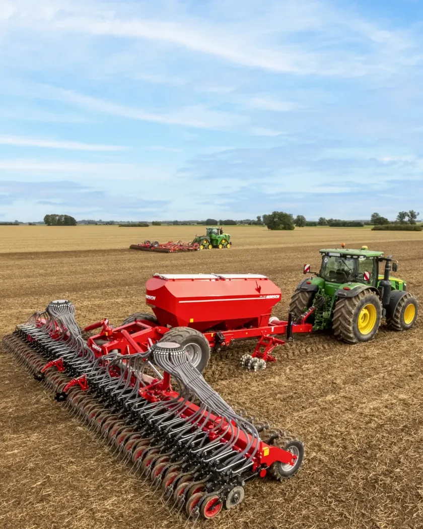 Sembradora Horsch Serto desplegada a tota amplada darrere d'un tractor verd, en un camp de rostoll