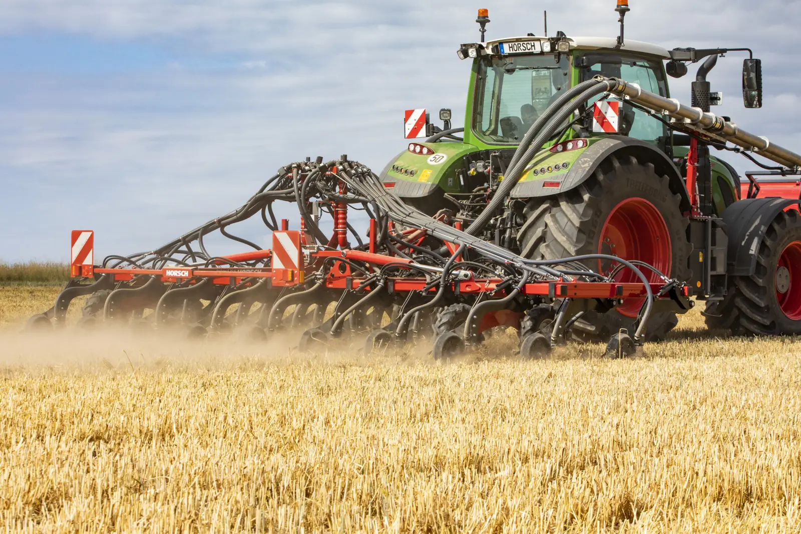 Sembradora Horsch Sprinter aixecant pols darrere d'un tractor verd, en un camp de rostoll