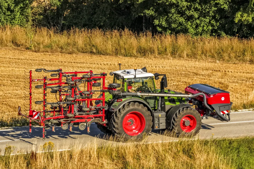 Tractor verd amb l'Sprinter plegada i la tremuja vermella, circulant per una carretera
