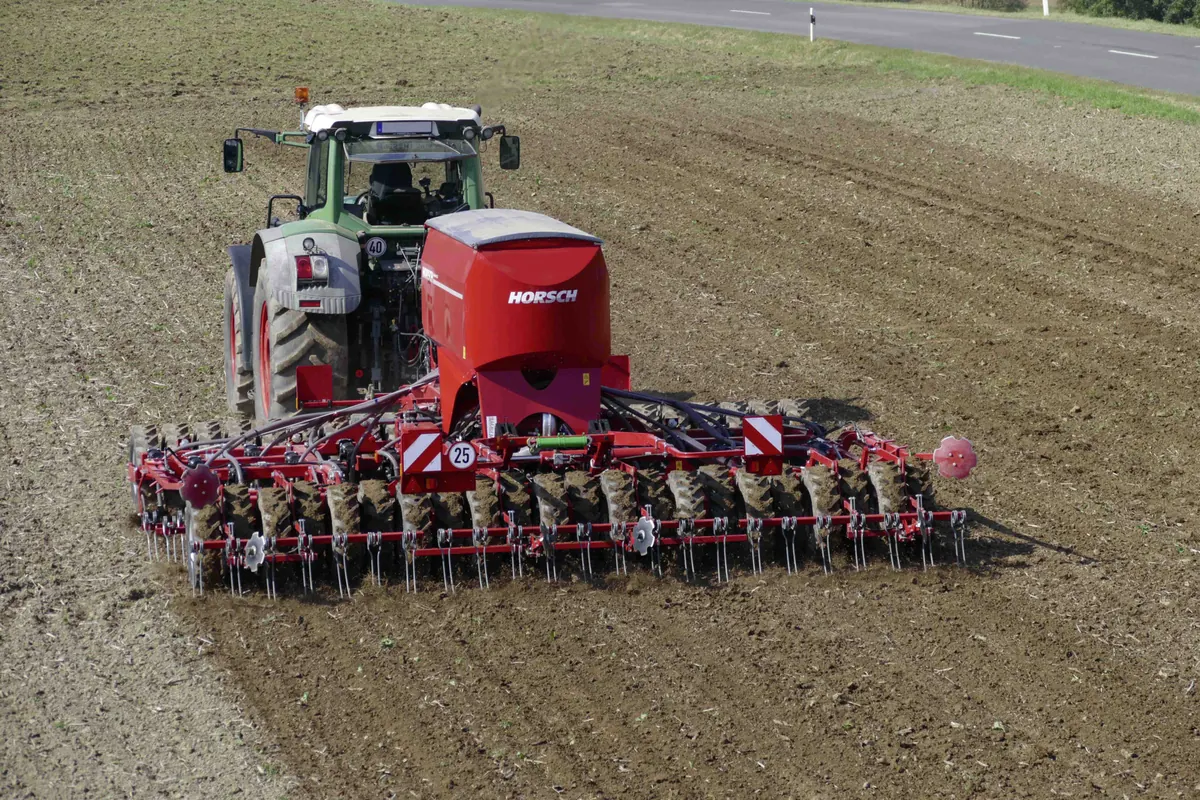 Vista des de dalt d'un tractor verd amb l'Sprinter i la tremuja treballant al costat d'una carretera