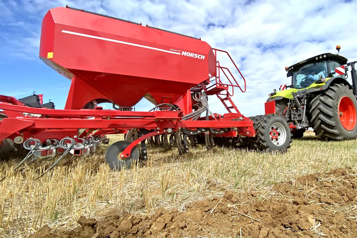 Primer pla de la tremuja vermella de l'Sprinter amb el tractor al costat, sobre terra oberta