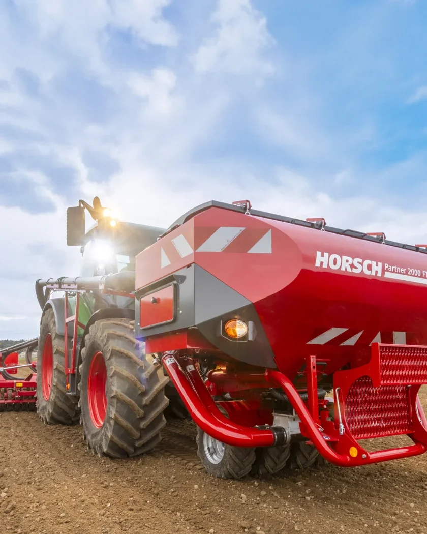 Tremuja davantera Horsch Partner 2000 FT en primer pla, al davant d'un tractor verd amb la Taro enganxada al darrere, sobre un camp treballat