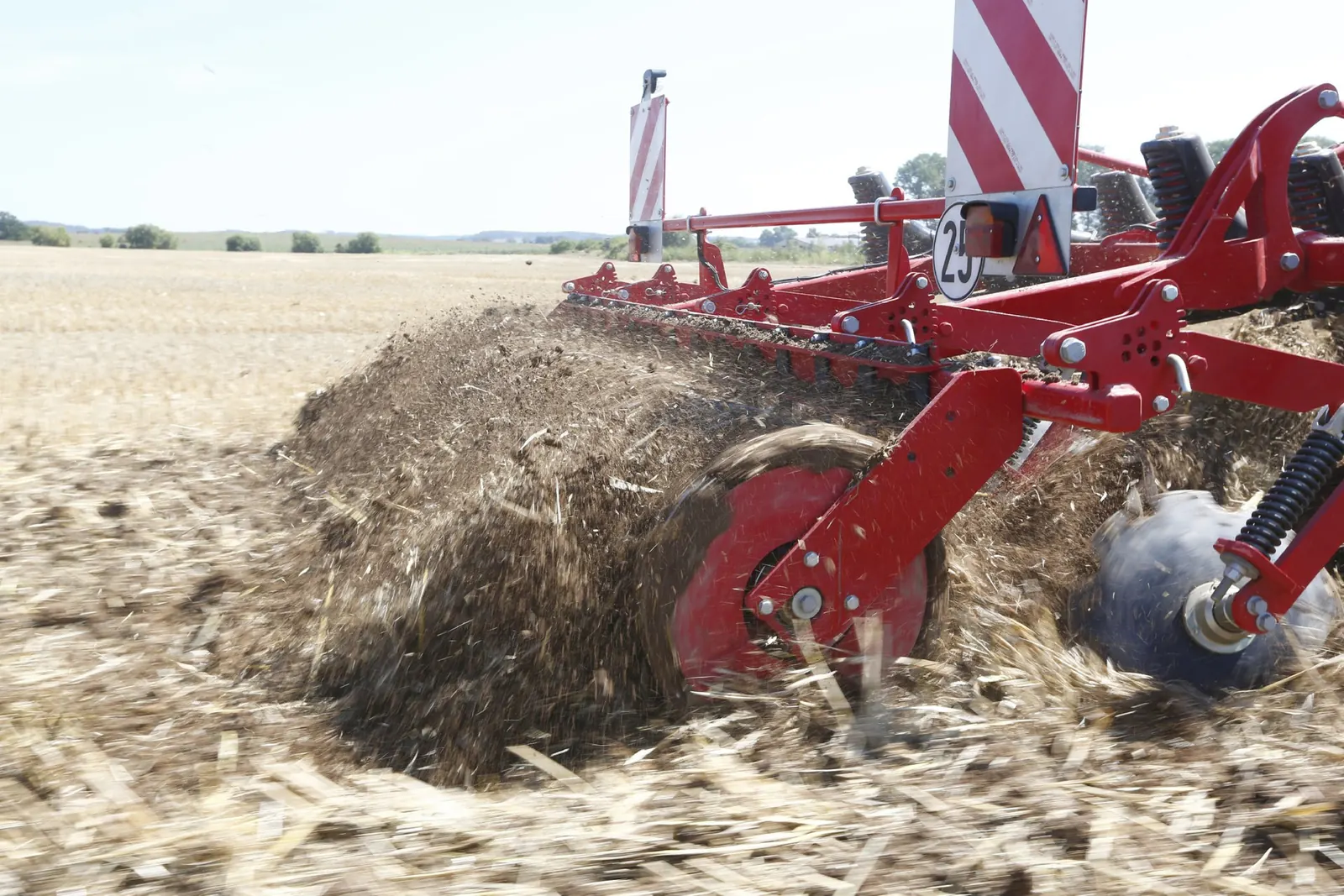 Primer pla dels discos anivelladors del cultivador llançant una ona de terra i palla sobre el rostoll