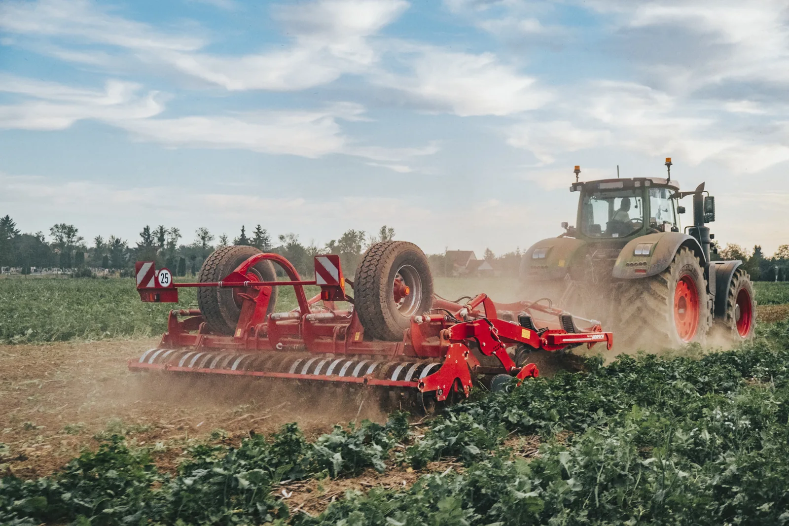 Cultivador Horsch Tiger treballant amb pols, amb el tractor verd al capdavant i el bosc al fons