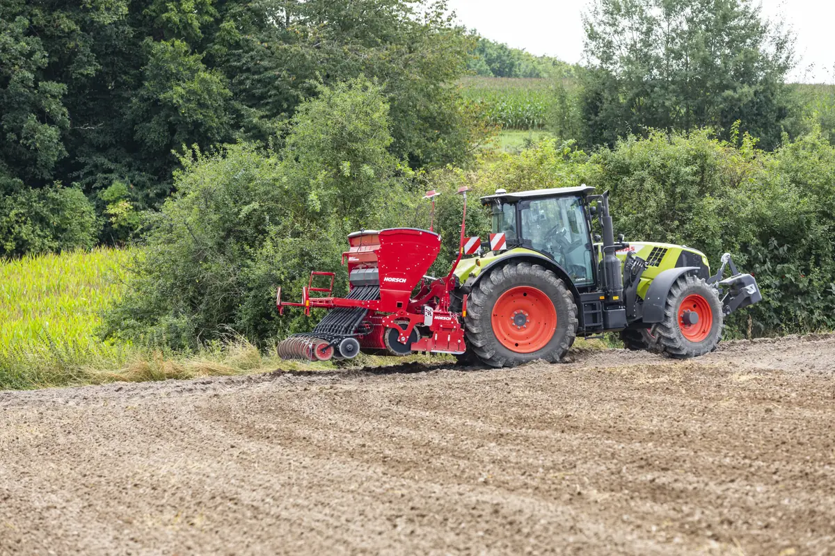 Tractor amb una Versa enganxada a la vora d'un camp treballat, al costat d'una bardissa