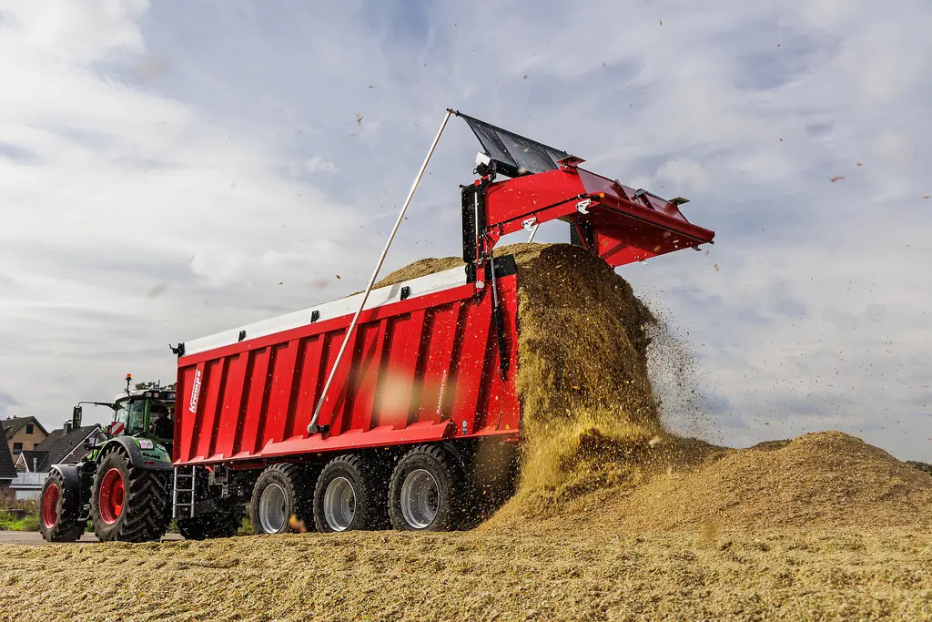 Remolc Krampe RamBody de tres eixos buidant farratge picat amb la porta del darrere aixecada, amb el tractor al costat