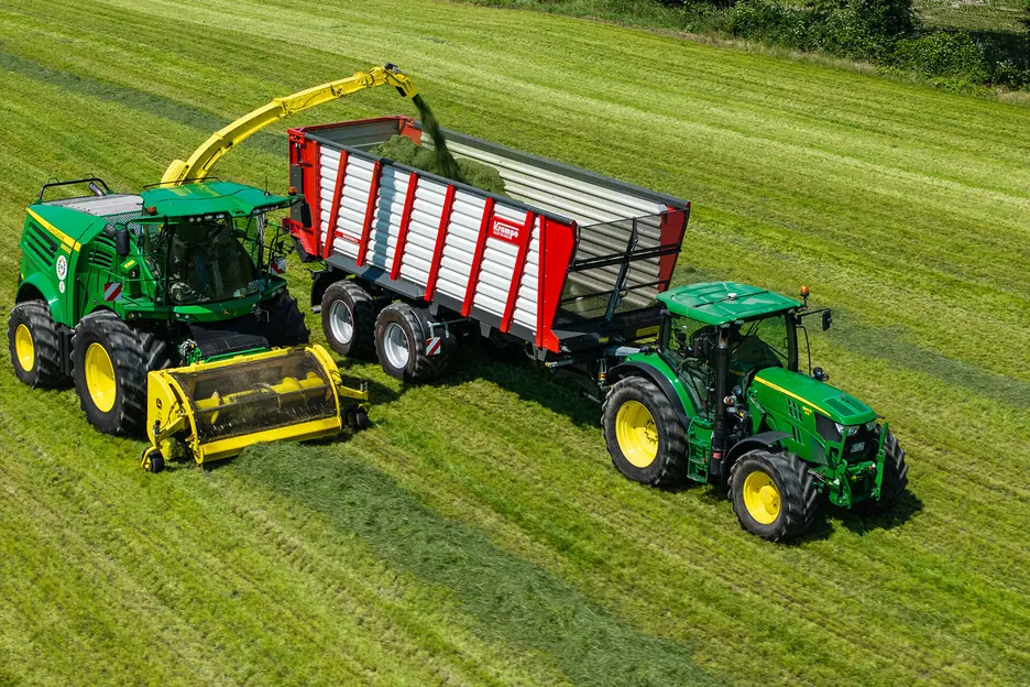 Vista aèria d'una picadora carregant herba dins d'un remolc Krampe Radium estirat per un tractor verd