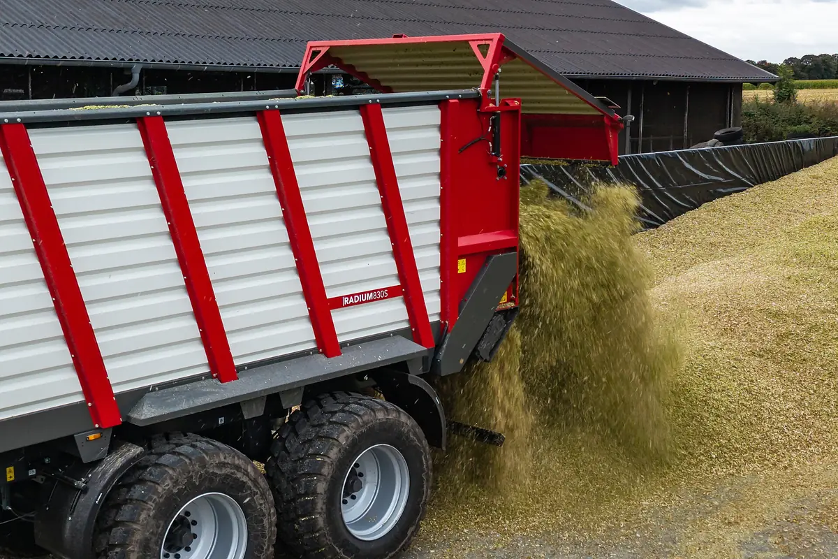 Remolc Krampe Radium buidant herba picada pel darrere al costat d'un silo i una nau