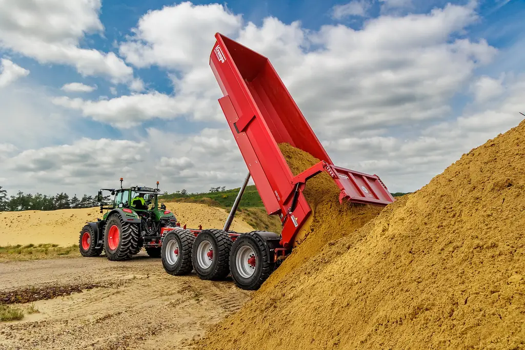 Bolquet Krampe HD 700 de tres eixos amb la caixa aixecada del tot abocant sorra, amb el tractor a l'esquerra