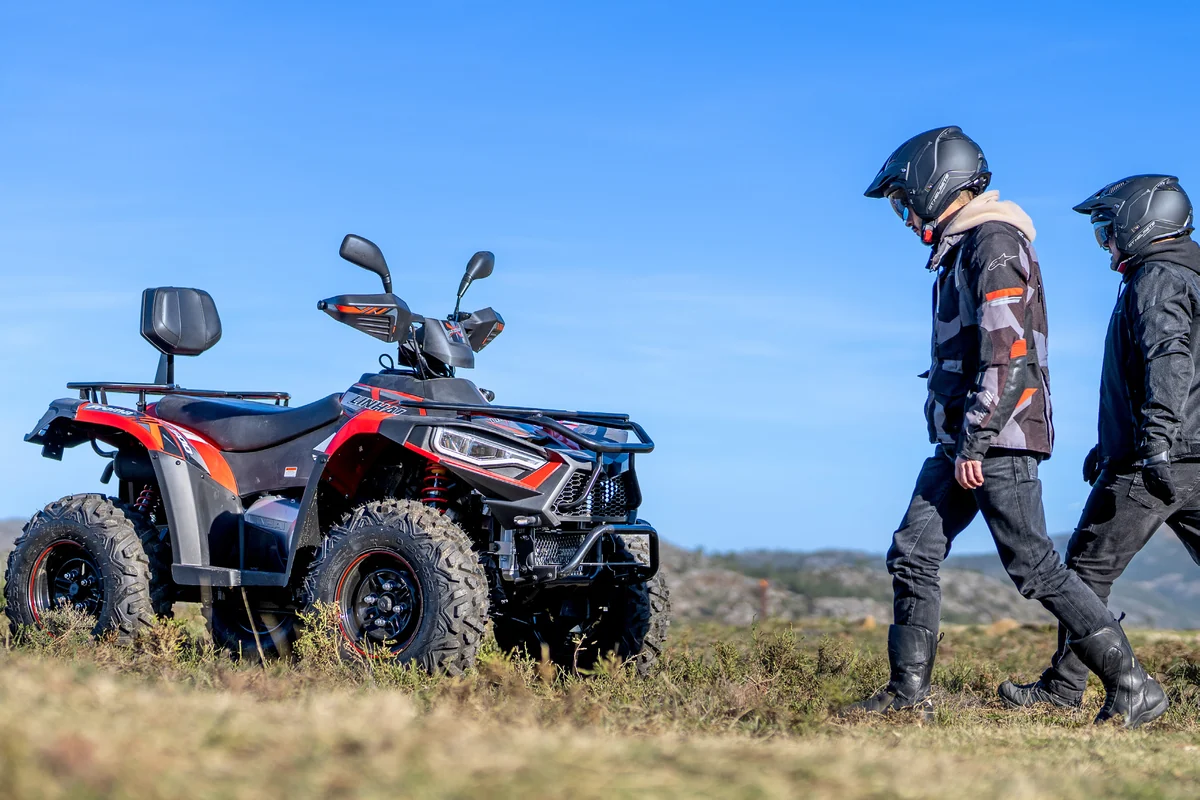 Quad Linhai negre i vermell aturat dalt d'un turó, amb dues persones amb casc i equip de conducció caminant cap a ell