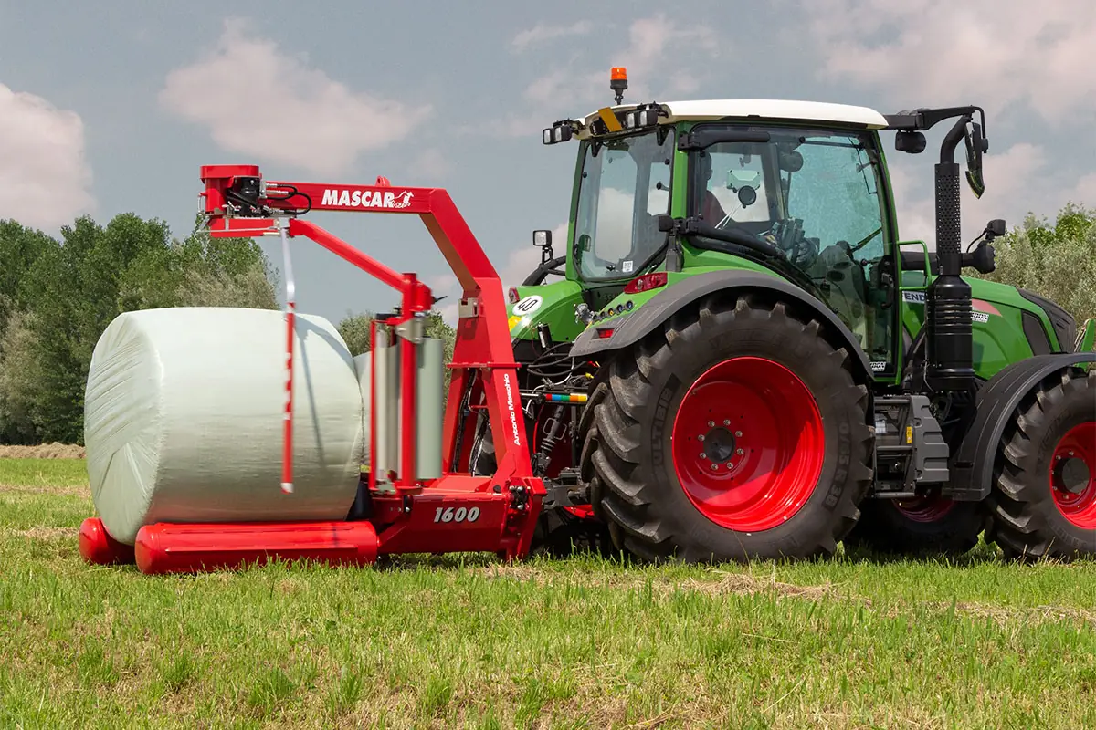 Encintadora Mascar 1600 vermella amb una bala acabada d'embolicar amb film blanc, i un tractor verd al costat