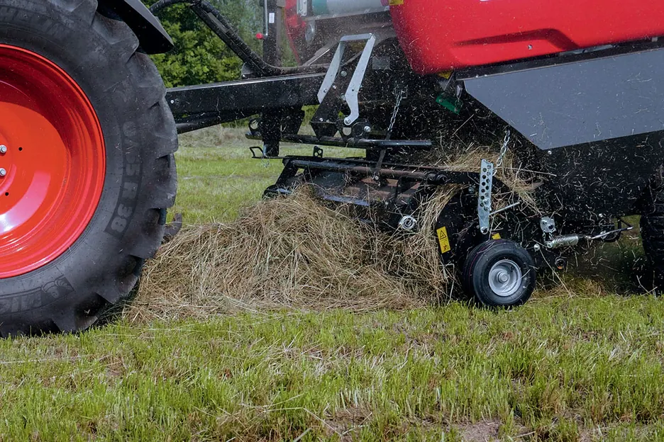 Primer pla del recollidor de pues aixecant l'herba del terra, amb la roda del tractor al costat