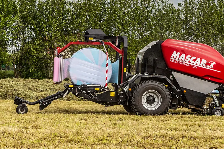 Multiwrap 130 encintant una bala amb film rosa en un prat, amb arbres al fons