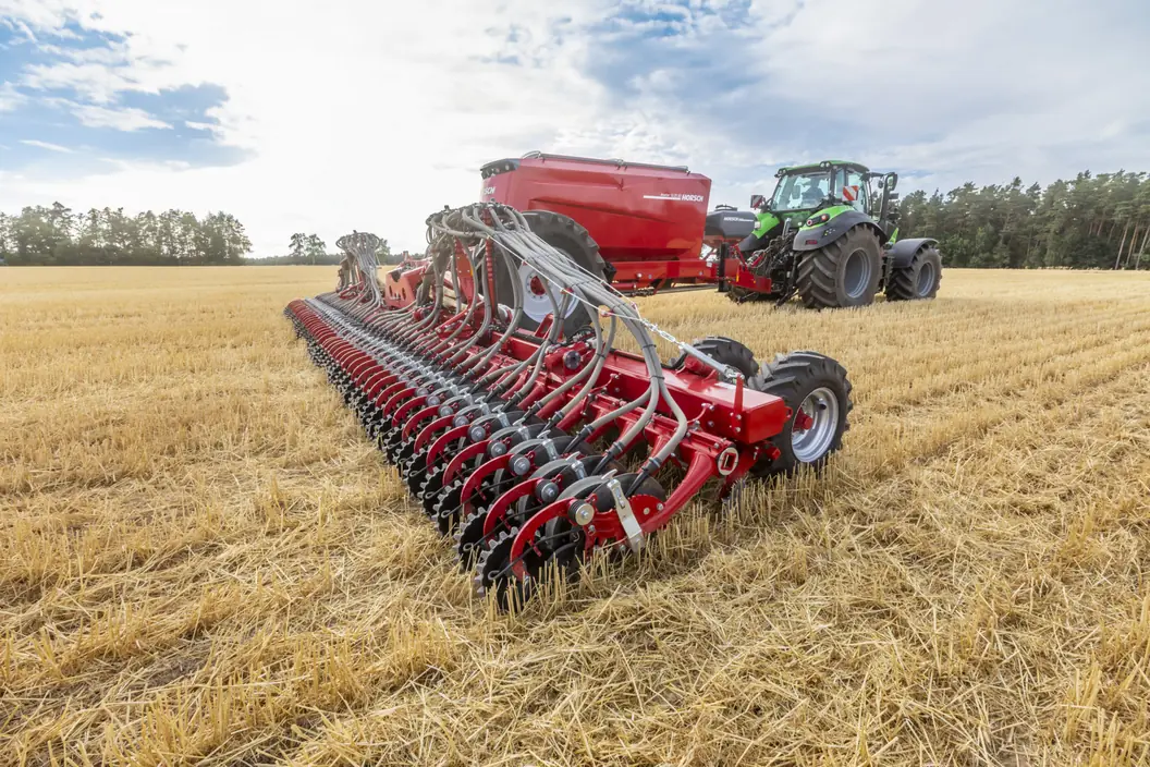 Sembradora Horsch Avatar SD amb la filera de relles de disc desplegada sobre el rostoll, amb el tractor i la tremuja al fons